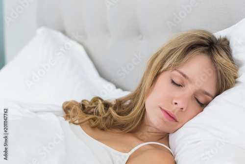 Foto Adult female lying on bed on right side, resting head on white pillow, wearing c