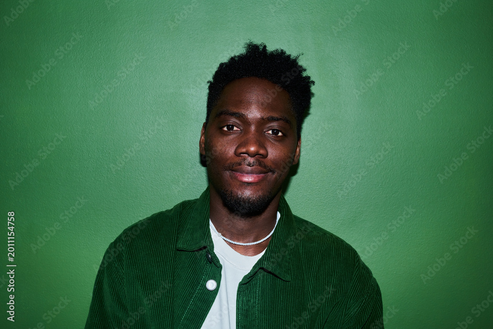Naklejka premium Portrait of young Black man looking at camera against green background, conveying confidence and authenticity. Ideal for diversity marketing, personal branding, profile use