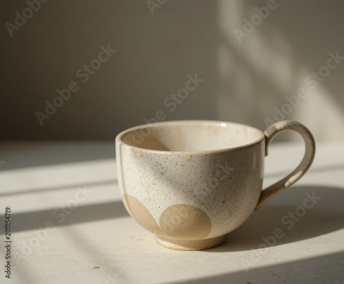 A simple ceramic coffee cup placed on a neutral surface with soft natural sunlight casting shadows. Minimalist composition emphasizing calmness, warmth, and daily routine. 
