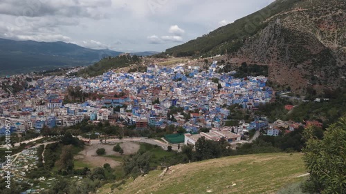 Panoramic view of Chefchaouen, the famous Blue Pearl of Morocco, nestled in the green Rif Mountains under a cloudy sky