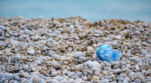 Obraz na plátně Crushed blue plastic water bottle littered on a pristine natural pebble beach