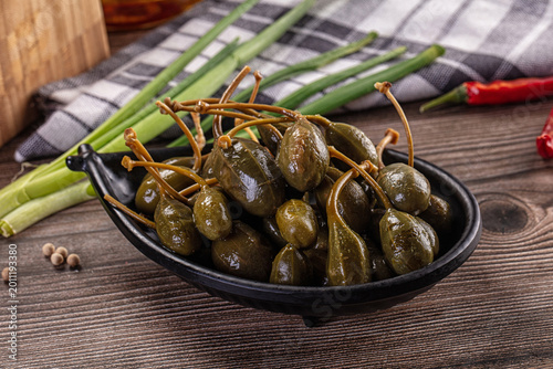 Bilde på lerret Pickled caper berries in a bowl with fresh ingredients on a rustic wooden table