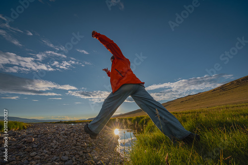 Foto Energetic person jumping over a mountain stream during golden hour sunset, symbo
