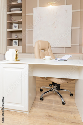 Beige leather chair, laptop and desk in office.Modern workplace.Stylish workplace with laptop, cup of coffee. elegant personal accessories in home decor.