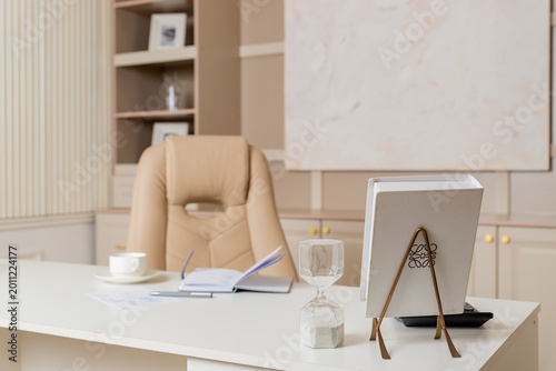 Beige leather chair, laptop and desk in office.Modern workplace.Stylish workplace with laptop, cup of coffee. elegant personal accessories in home decor.
