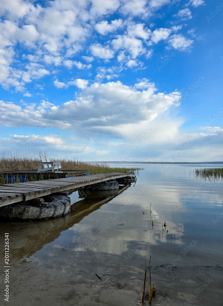 Obraz premium Wooden pier on a calm lake under a blue sky with clouds