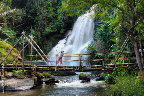 Woman traveling enjoying waterfall view from bamboo bridge in thailand