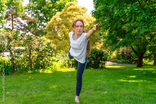 Obraz na płótnie Woman practices yoga pose outside in green park during sunny day