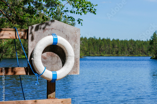 White lifebuoy on a wooden stand by a forest lake. Water safety and rescue concept