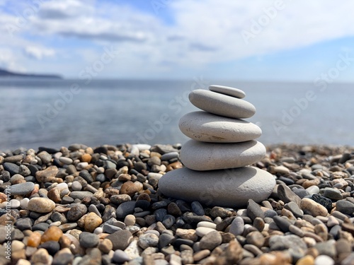 Photography a serene, low-angle close-up of five smooth, light-grey stones carefully stacked in perfect balance on a pebble beach