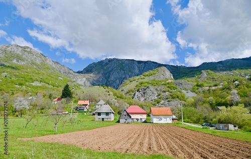 Fotografia Scenic rural landscape with a freshly ploughed field, small village houses, and lush green mountains under a cloudy sky