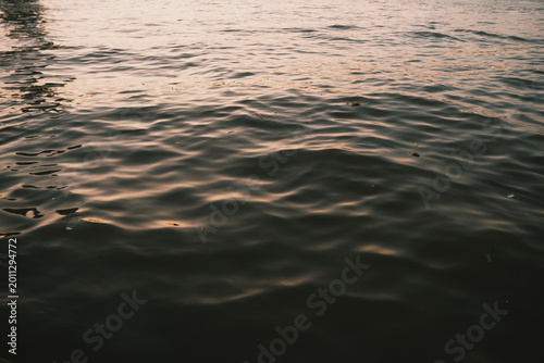 Canvas Print Serene close-up view of calm water at golden hour, featuring gentle ripples across the surface with beautiful warm pink, orange, and golden reflections from the sunset or sunrise