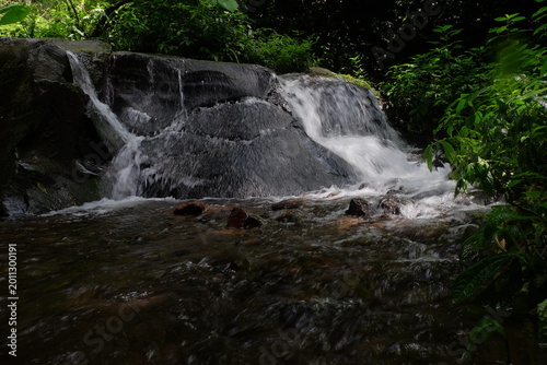 beautiful waterfall with trees and coral. water flows over dark, rugged stones, rocks creating staircase effect. The scene is serene natural landscape.