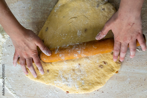 Tableau sur toile Person presses timber tool against soft elastic yeast pastry containing raisins