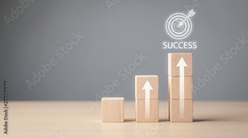 Wooden blocks stacking as a staircase with an arrow pointing up to a target icon and the word success, representing business growth and achievement