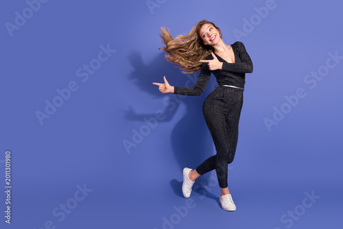 Tablou pe pânză Young woman in striped jumpsuit dances against a violet background smiling and p