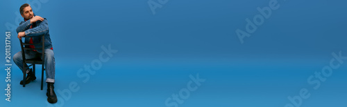 Tableau sur toile Stylish adult man posing thoughtfully on a chair against a vibrant blue backdrop