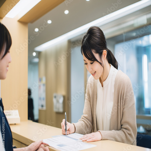 市役所窓口で書類提出する笑顔の30代日本人女性と女性職員 行政サービスイメージ