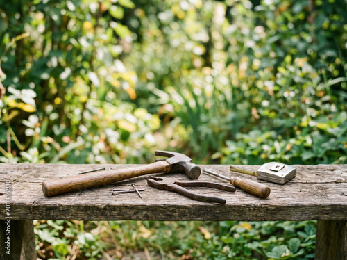 Rustic hand tools on weathered wooden bench in garden setting with hammer pliers tape measure and nails for diy workshop background and outdoor repair scene