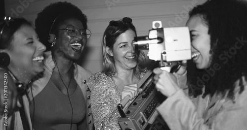 Group of multiracial girls having fun dancing and listening music together while using vintage film camera outdoor - Party, nightlife and people lifestyle concept - Black and white editing