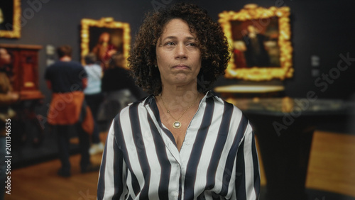 Cuadro en lienzo Middle aged woman in striped blouse gazes at ornate classical painting in modern building interior; uncertainty