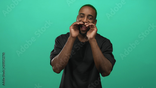 Fotografie Man cupping hands to mouth calling and smiling with visible braces in studio against a teal green backdrop; joyful energy