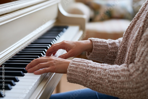 Close-up of piano keyboard with student hands, beige and white color palette.