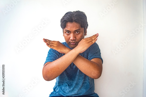 A man in a blue shirt makes a prohibitive gesture with crossed arms and open hands, against a plain white background