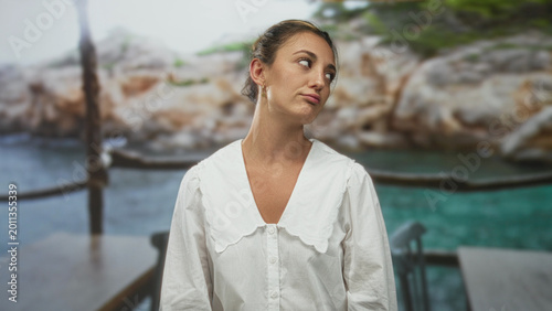 Foto Woman tilts head and looks up showing neck and collarbone in studio with seaside backdrop and wooden railing; quiet contemplation