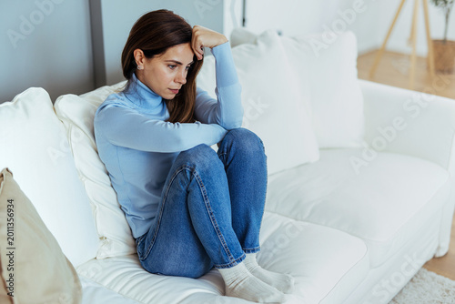 Pensive Young Woman Sitting on Couch Looking Worried and Anxious at Home
