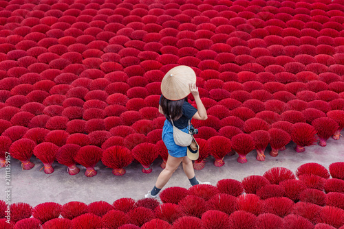 Young female traveler with traditional conical hat walking through red incense sticks in Quang Phu Cau village, Vietnam