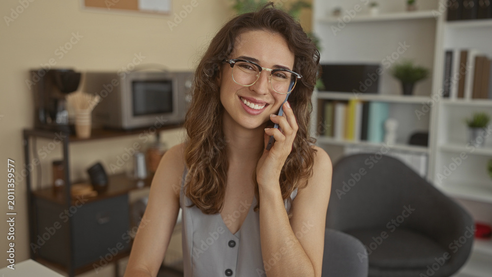Fototapeta premium Young woman wearing glasses holds smartphone to ear in building with focused expression; connection happiness.