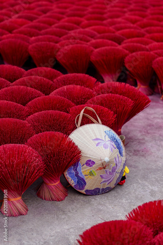 Traditional Vietnamese conical hat with floral painting leaning against bundles of red incense sticks