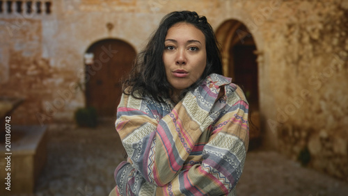 Tableau sur toile Woman with arms crossed over chest in building ruins wearing patterned jacket and looking down; melancholy solitude