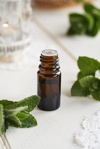 A bottle of essential oil with peppermint leaves on white background