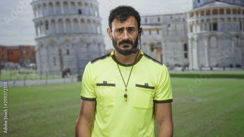 Tableau sur toile Man referee in neon yellow shirt with whistle on neck, tilting head and frowning near building; frustration