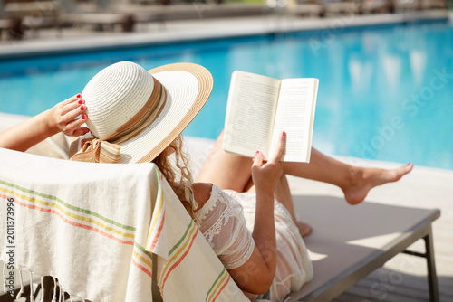 Foto Woman reading book by poolside relaxing during summer vacation