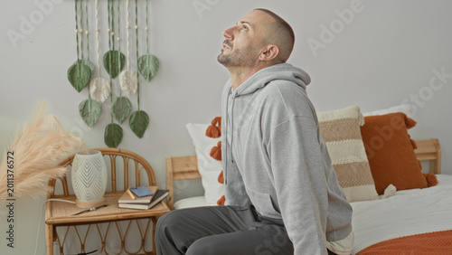 Quadro em tela Man sitting on bed in studio with hand on head gripping temple after waking, showing pained expression and restless posture; pain