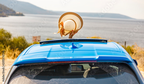 Foto Woman holding sun hat out of car sunroof by seaside road