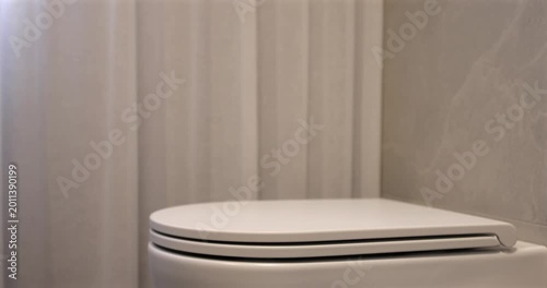 Soft close toilet lid in modern bathroom, static interior video captures white ceramic fixture as seat lowers gently in natural daylight beside sheer curtain creating clean quiet domestic scene