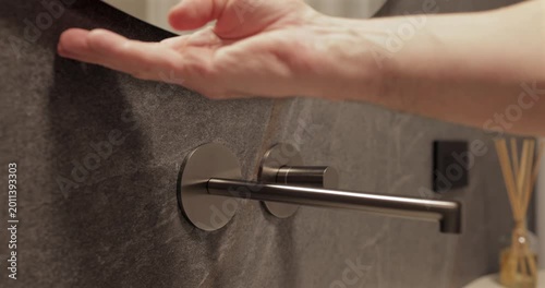 Touchless lighting activation under modern mirror with soft halo glow, static bathroom footage focuses on palm gesture that switches integrated backlight above textured stone and sleek premium sink