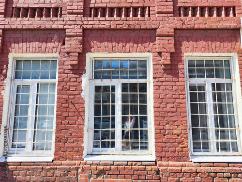 Building wall with three windows showcasing red brick pattern and metal bars in bright sunlight during daytime in urban area
