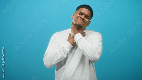 Tableau sur toile Hispanic man clutching throat with both hands in a blue studio backdrop, grimacing and gagging; pain struggle