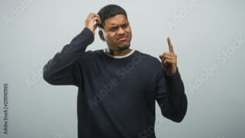 Tableau sur toile Hispanic man scratches head and points index finger upward in studio; confusion thought curiosity perplexity