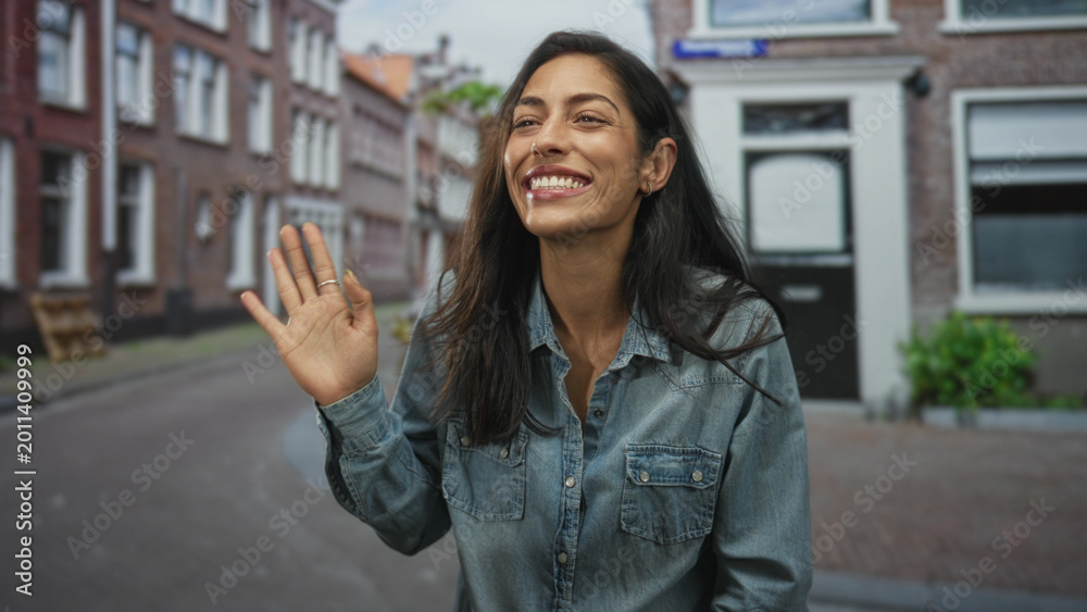 Fototapeta premium Woman smiling and holding hair with hand on a narrow street lined with brick buildings; joy candid moment.