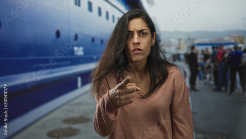 Fotografija Woman frowning with furrowed brow standing near a ship at port under overcast sky; frustration solitude travel