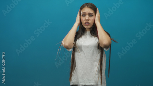 Foto Teen girl covers ears with hands in studio against a blue backdrop, eyes closed and tense posture; anxiety distress isolation