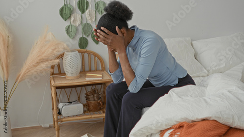 Foto Woman seated on bed covering her face with hands while leaning forward in a styled bedroom studio with bedding and nightstand details; anxiety