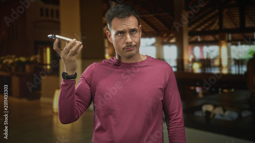 Konstfotografi Man with moustache wearing pink long sleeve shirt holds smartphone to ear with right hand and furrows brow in a building reception; annoyance waiting