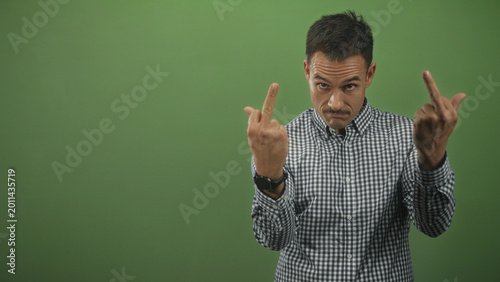 Foto Hispanic man flipping middle finger with both hands in green studio; defiance irreverence contempt attitude
